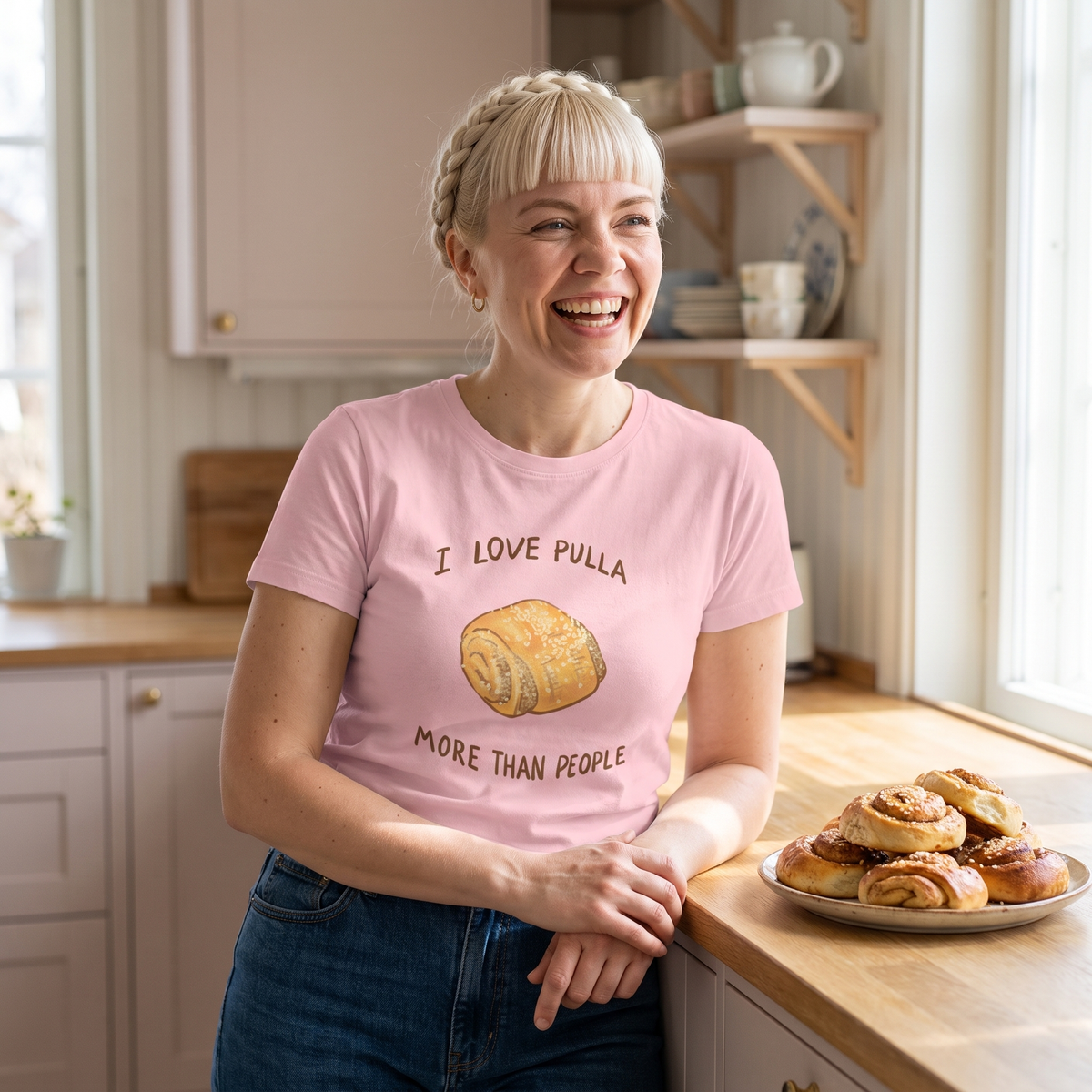 I Love Pulla More Than People t-shirt in pink, worn by Venla laughing in a pastel kitchen, Very Finnish Problems
