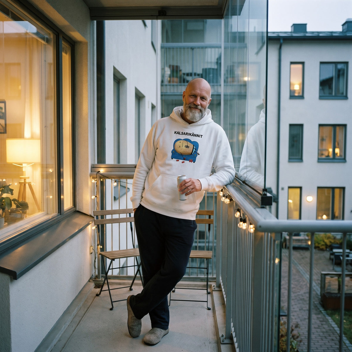 Kalsarikännit hoodie in white, worn by a bearded man leaning on a glazed apartment balcony, Very Finnish Problems