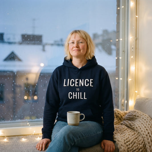 License to chill Finnish Winter Hoodie in navy, worn by Marika on a window seat on a snowy evening, Very Finnish Problems