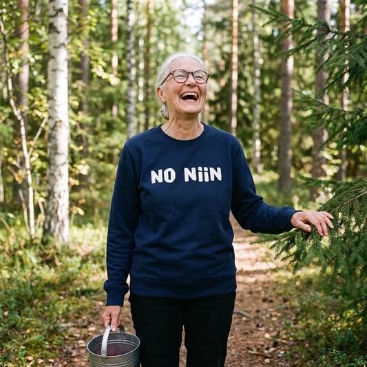 No niin eco-friendly Finnish language sweatshirt in French navy, worn by Raija laughing on a Finnish forest path, Very Finnish Problems