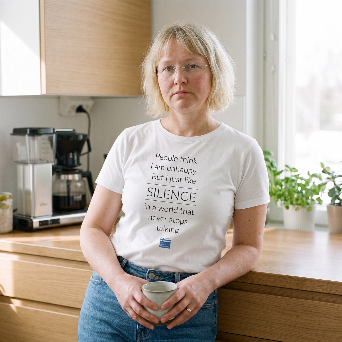 Not Unhappy Just Silent t-shirt in white, worn by Marika with a coffee in a quiet kitchen, Very Finnish Problems