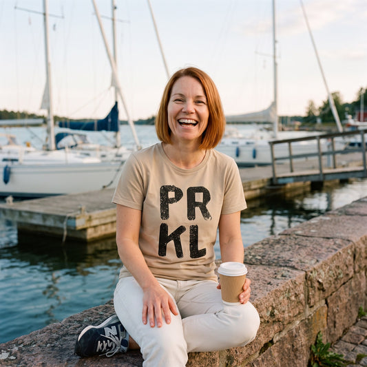 PRKL organic t-shirt in desert dust, worn by Sanna on a harbour wall, Very Finnish Problems