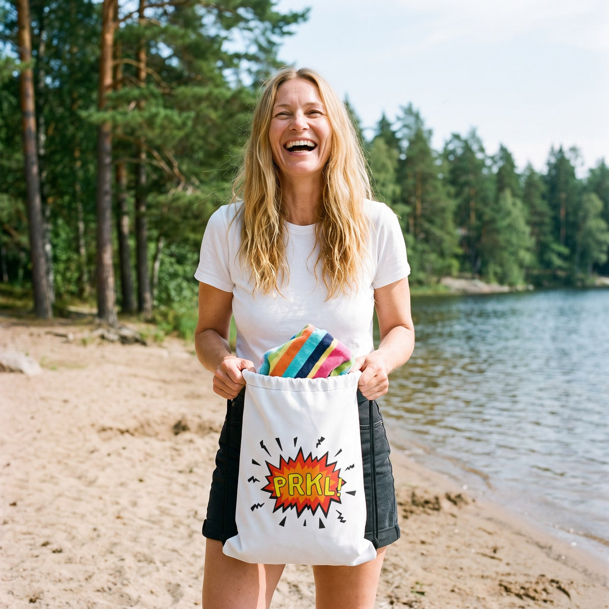 PRKL and PRKL Bang drawstring bag, held by Elina on a lake beach, PRKL Bang side, Very Finnish Problems