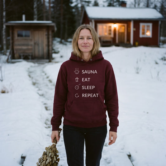 Sauna, Eat, Sleep, Repeat Finnish Lifestyle Hoodie in maroon, worn by Elina walking up from the sauna with a birch whisk, Very Finnish Problems