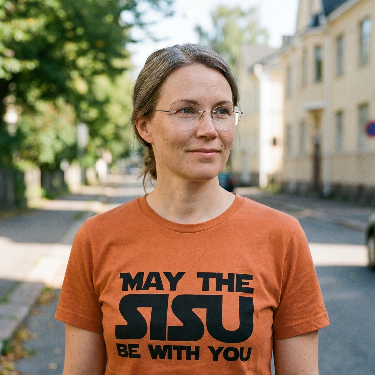 Woman on a Helsinki street wearing the burnt orange May the Sisu Be With You t-shirt, Very Finnish Problems