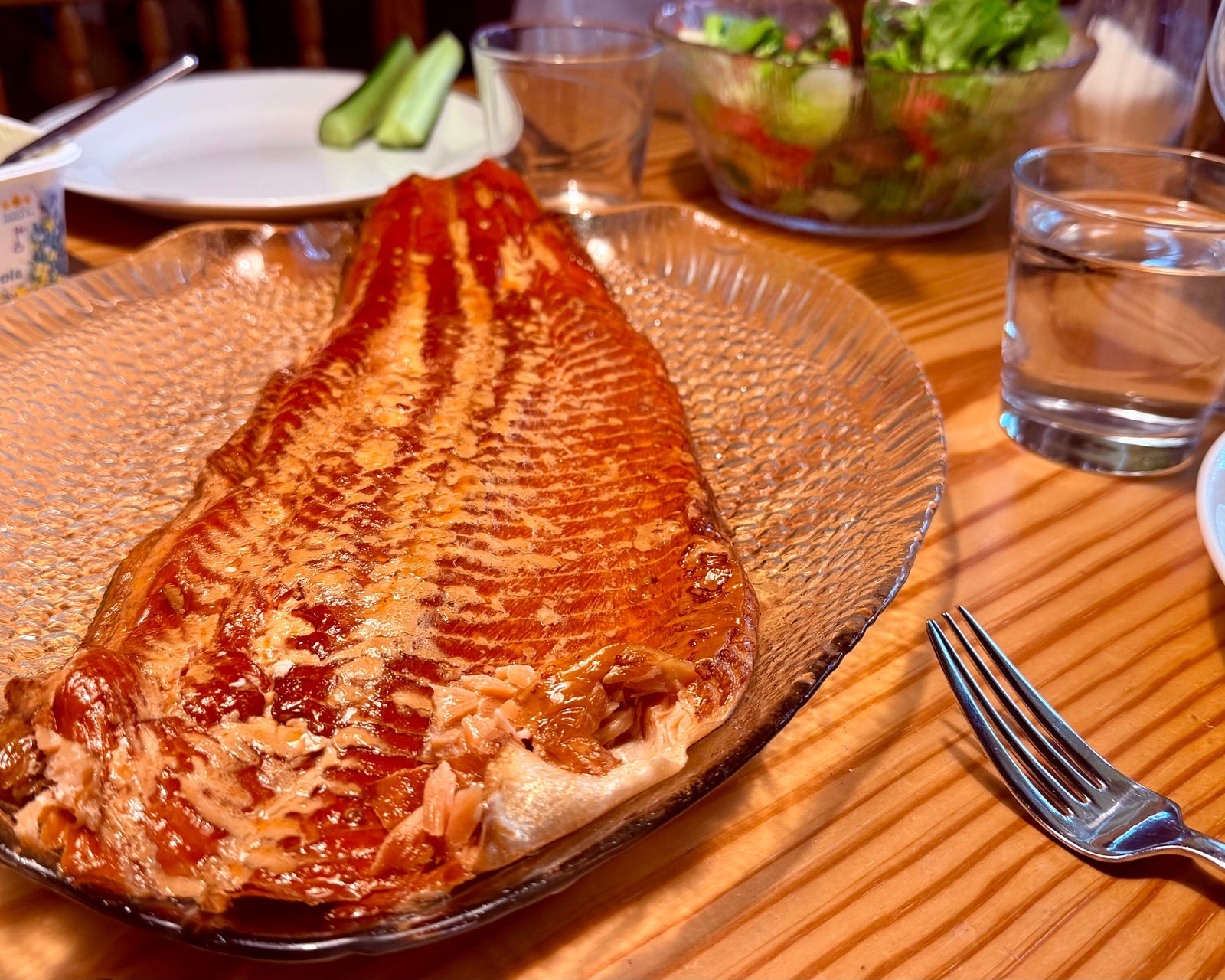 A whole side of smoked salmon on a glass platter on a Finnish table with salad and cucumber