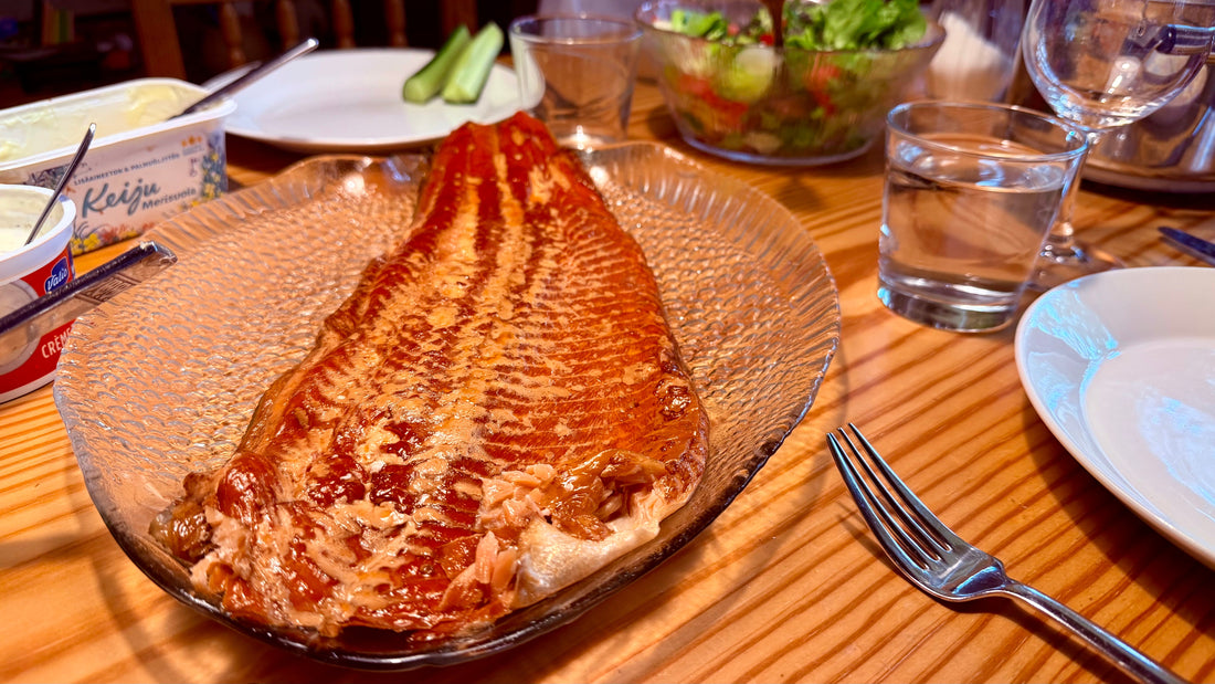 Whole hot-smoked salmon on a glass platter on a Finnish dinner table with salad and water glasses, photo by Joel Willans