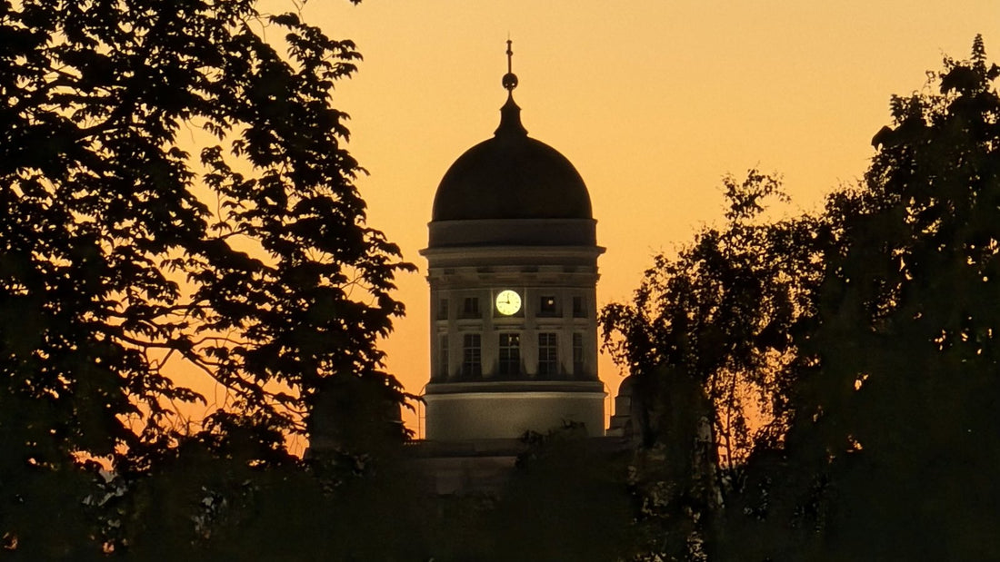The silhouetted dome and clock of Helsinki Cathedral framed by trees against an amber sunset sky