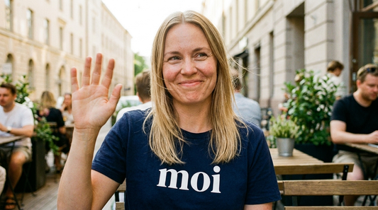 Finnish woman waving on a Helsinki summer terrace wearing the navy Moi t-shirt from Very Finnish Problems