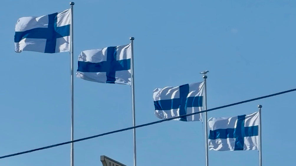 Four Finnish flags flying against a clear blue sky, photo by Joel Willans