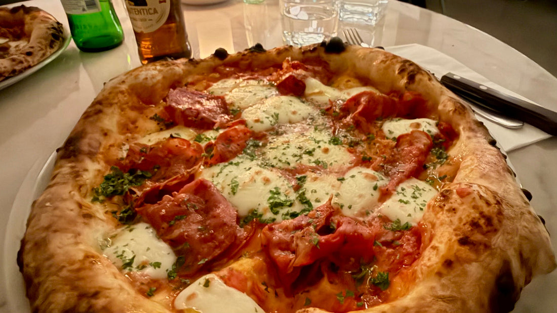 A wood-fired pizza topped with salami, mozzarella and herbs on a restaurant table, photo by Joel Willans