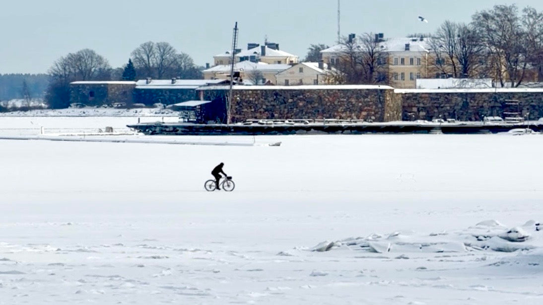 A lone cyclist riding across the frozen sea in front of snow-covered Suomenlinna fortress in Helsinki