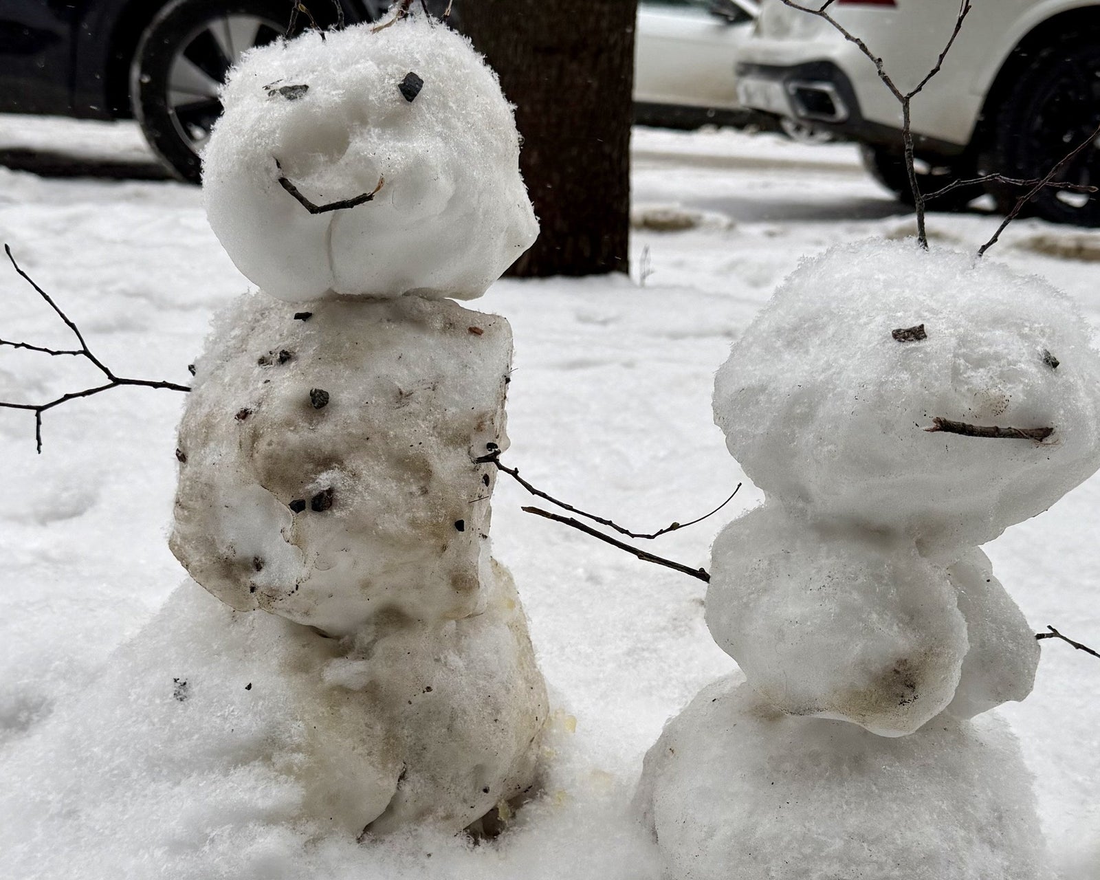 Two small melting snowmen with pebble faces standing on a Finnish street