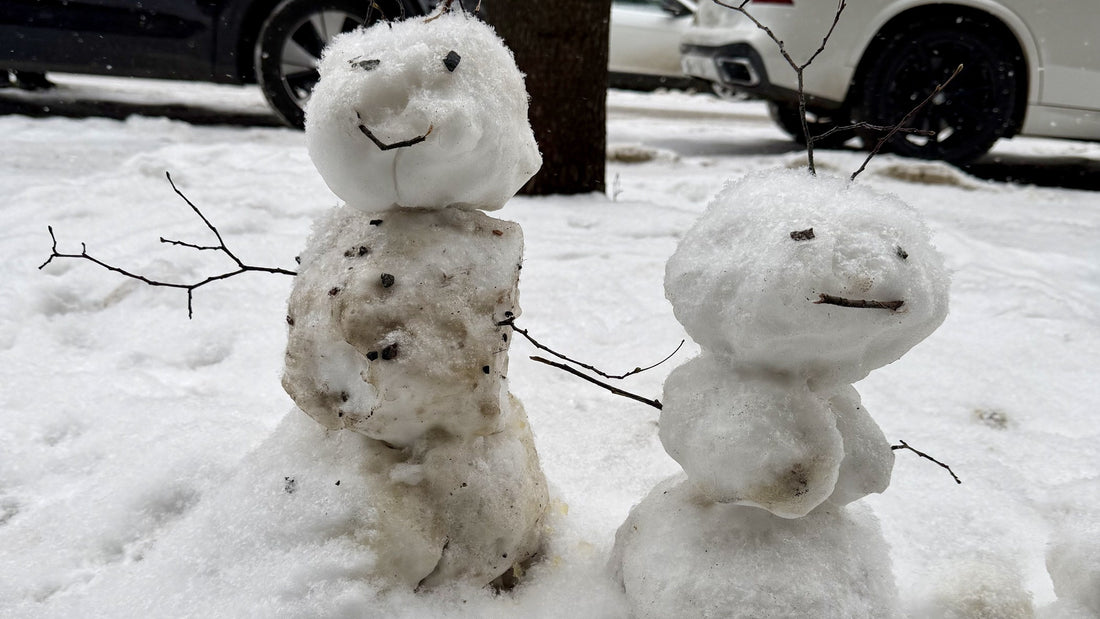 Two lopsided Finnish snowmen with twig arms on a snowy Helsinki street, photo by Joel Willans