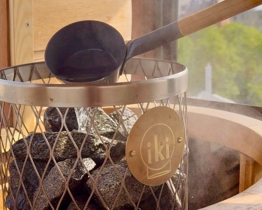 A ladle resting on an IKI kiuas sauna heater full of dark stones, steam drifting across a window. Photo: Joel Willans
