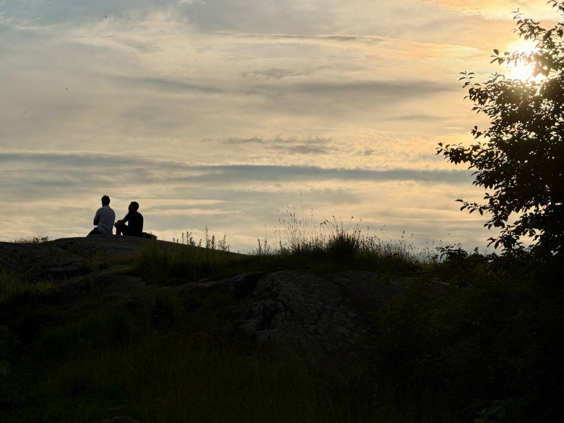 Two people sitting in comfortable silence on a rocky hill at sunset in Finland. Photo by Joel Willans