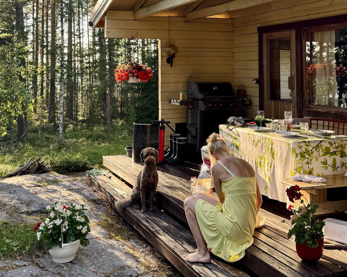 A Finnish summer cottage veranda with a laid table, a dog and family sitting out in the evening