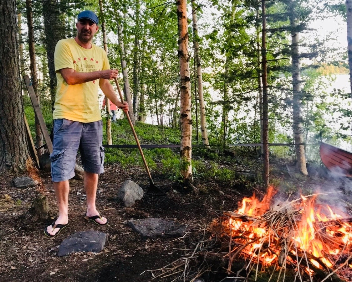 A man tending a large midsummer bonfire in a Finnish birch forest