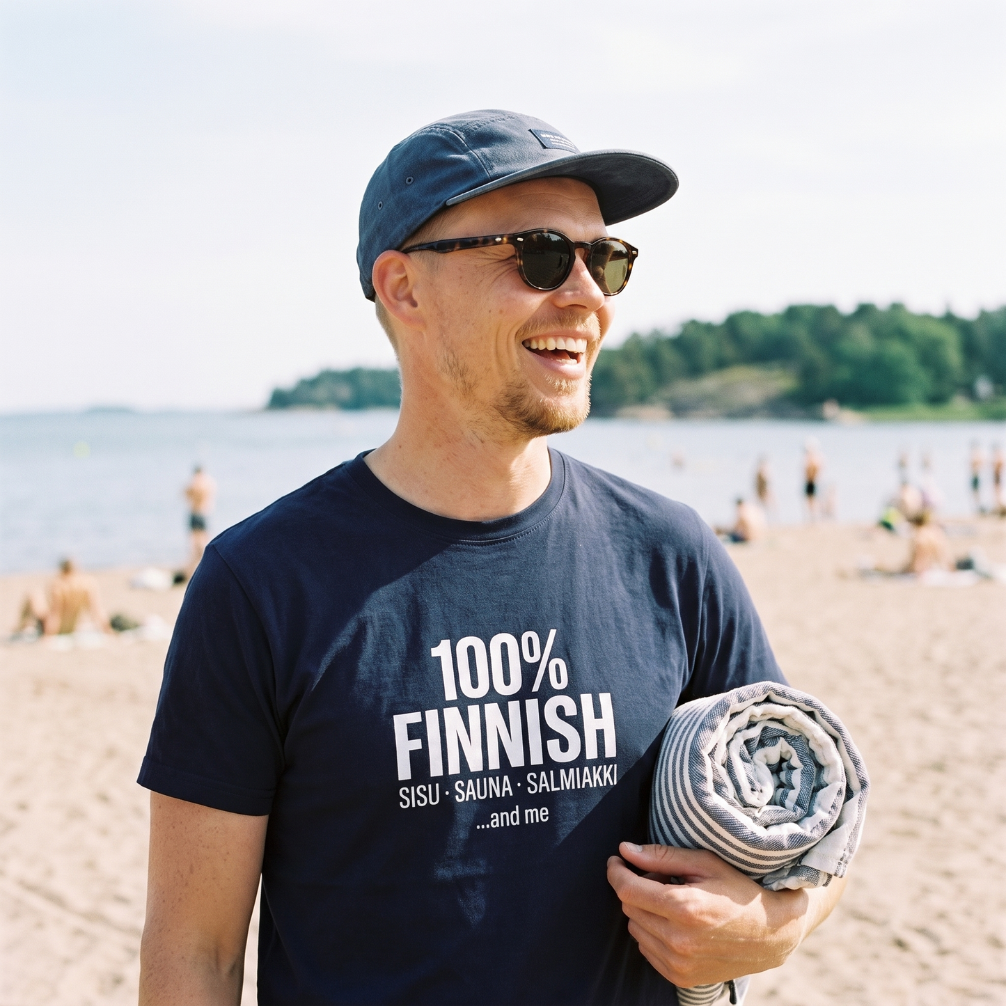 100% Finnish Sisu Sauna Salmiakki t-shirt in navy, worn by a man laughing on Hietaniemi beach in Helsinki, Very Finnish Problems