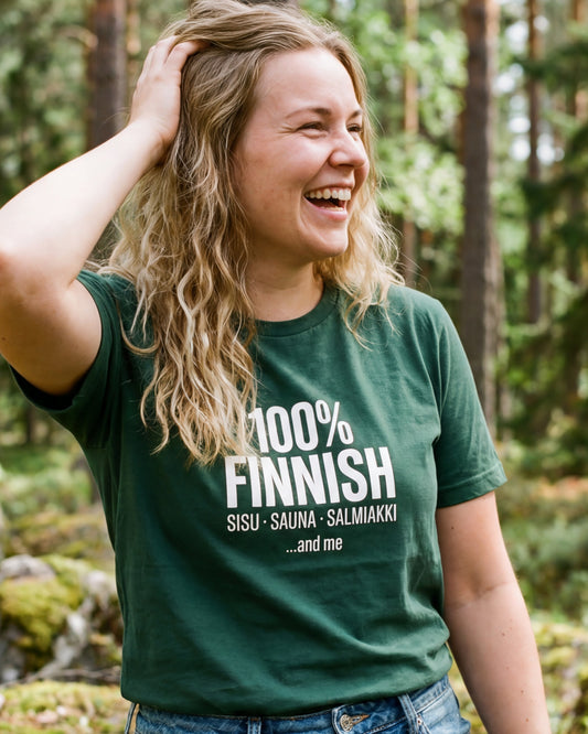 Woman laughing in a Finnish forest wearing the 100% Finnish Sisu Sauna Salmiakki t-shirt in forest green