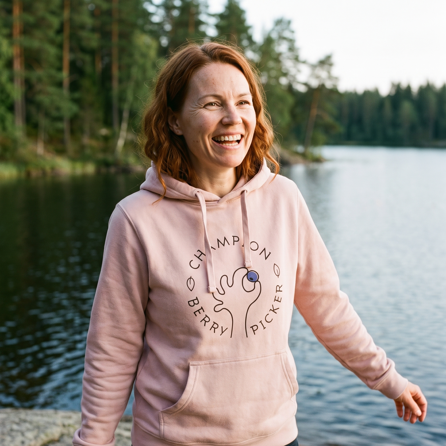 Champion Blueberry Picker hoodie in light pink, worn by Sanna on the granite shore of a forest lake, Very Finnish Problems