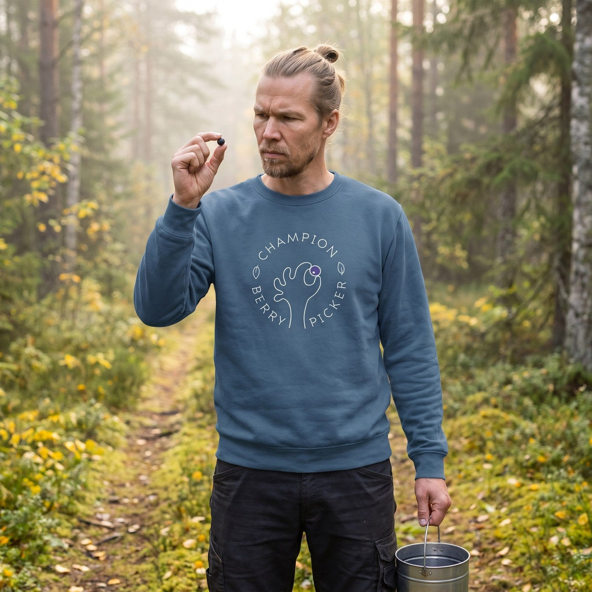 Champion Blueberry Picker sweatshirt in indigo blue, worn by Joonas inspecting a blueberry on a forest track, Very Finnish Problems