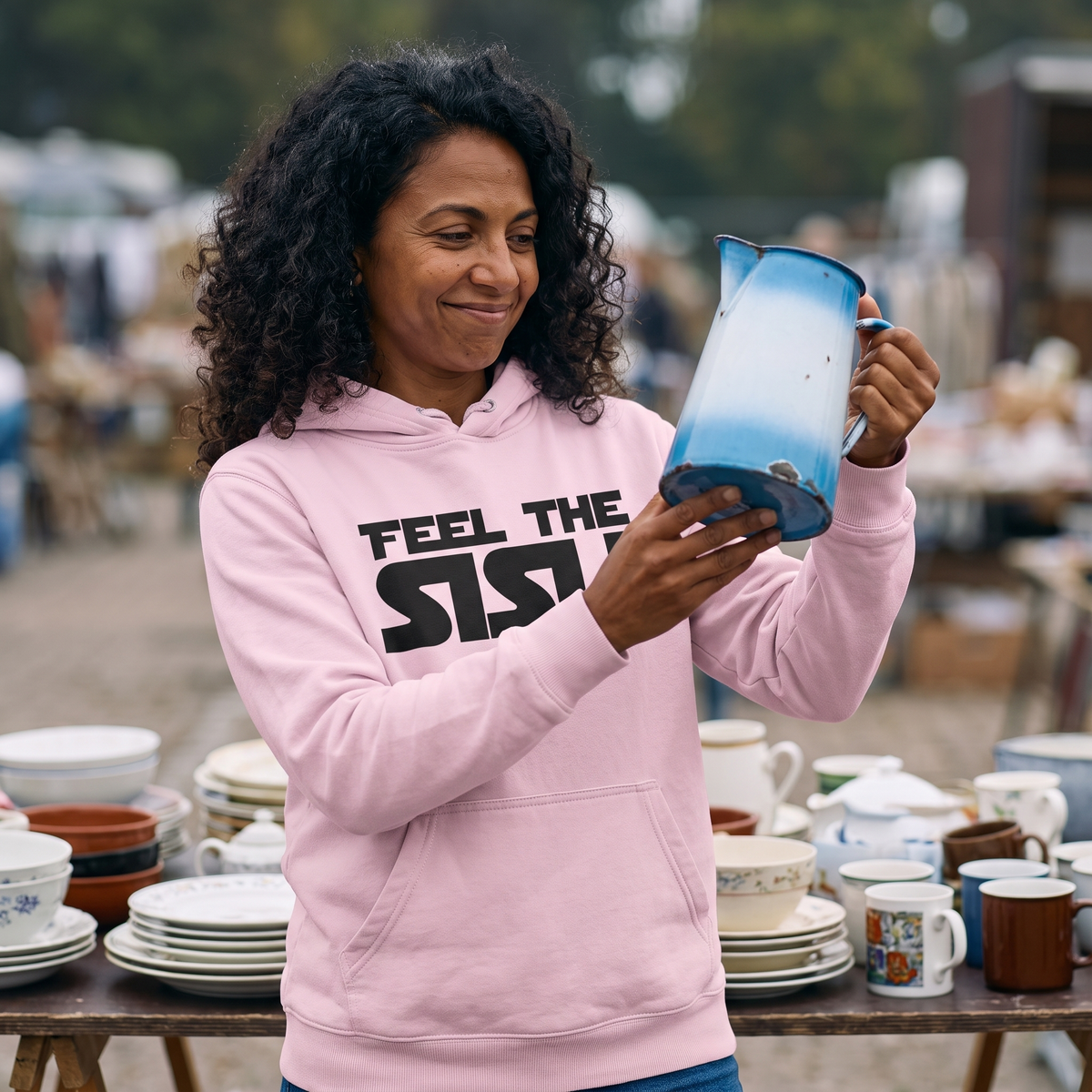 Feel the sisu Finnish culture hoodie in light pink, worn by Nea at a flea market stall, Very Finnish Problems