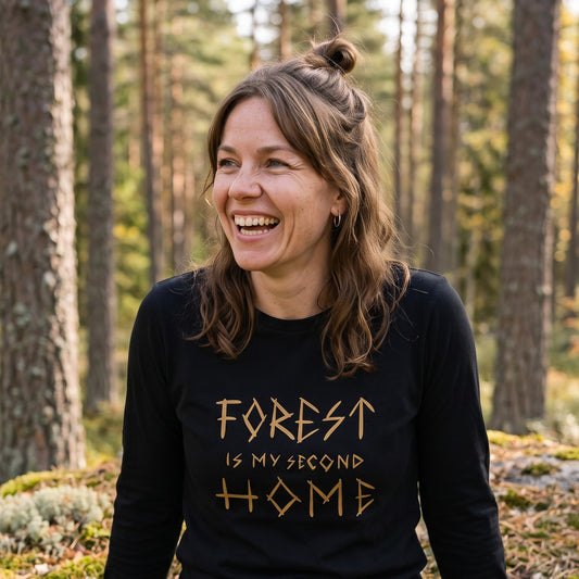 Forest Is Home long sleeve tee in black, worn by Suvi laughing on a mossy boulder in a pine forest, Very Finnish Problems