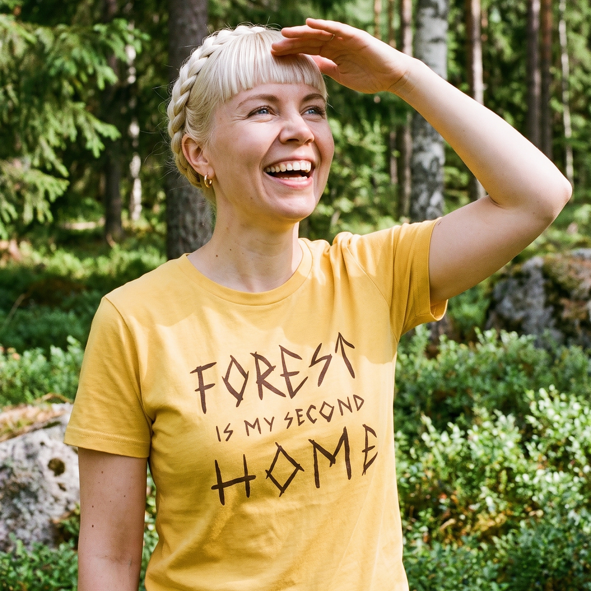 Forest Is Home t-shirt in yellow, worn by Venla in a sunlit Finnish forest clearing, Very Finnish Problems