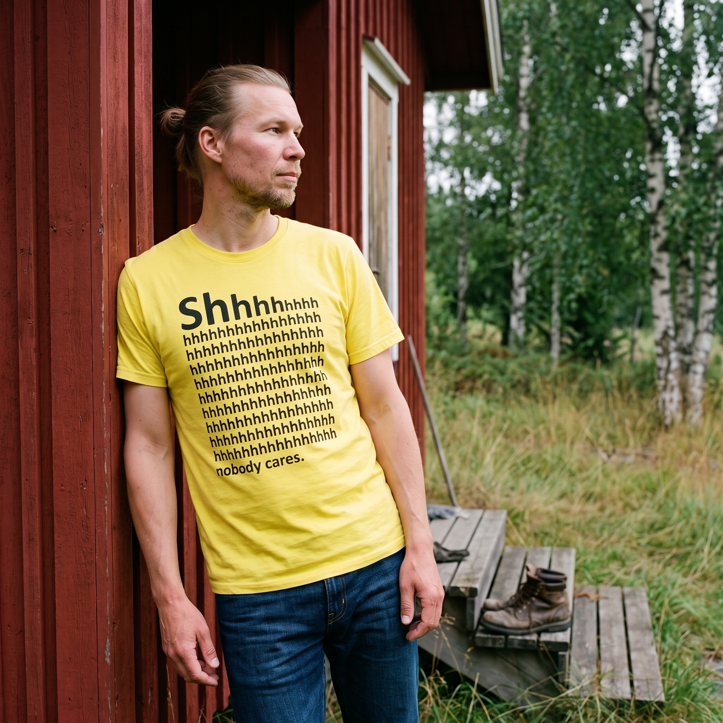 Shhh... Nobody Cares t-shirt in yellow, worn by a man at a cottage door, Very Finnish Problems