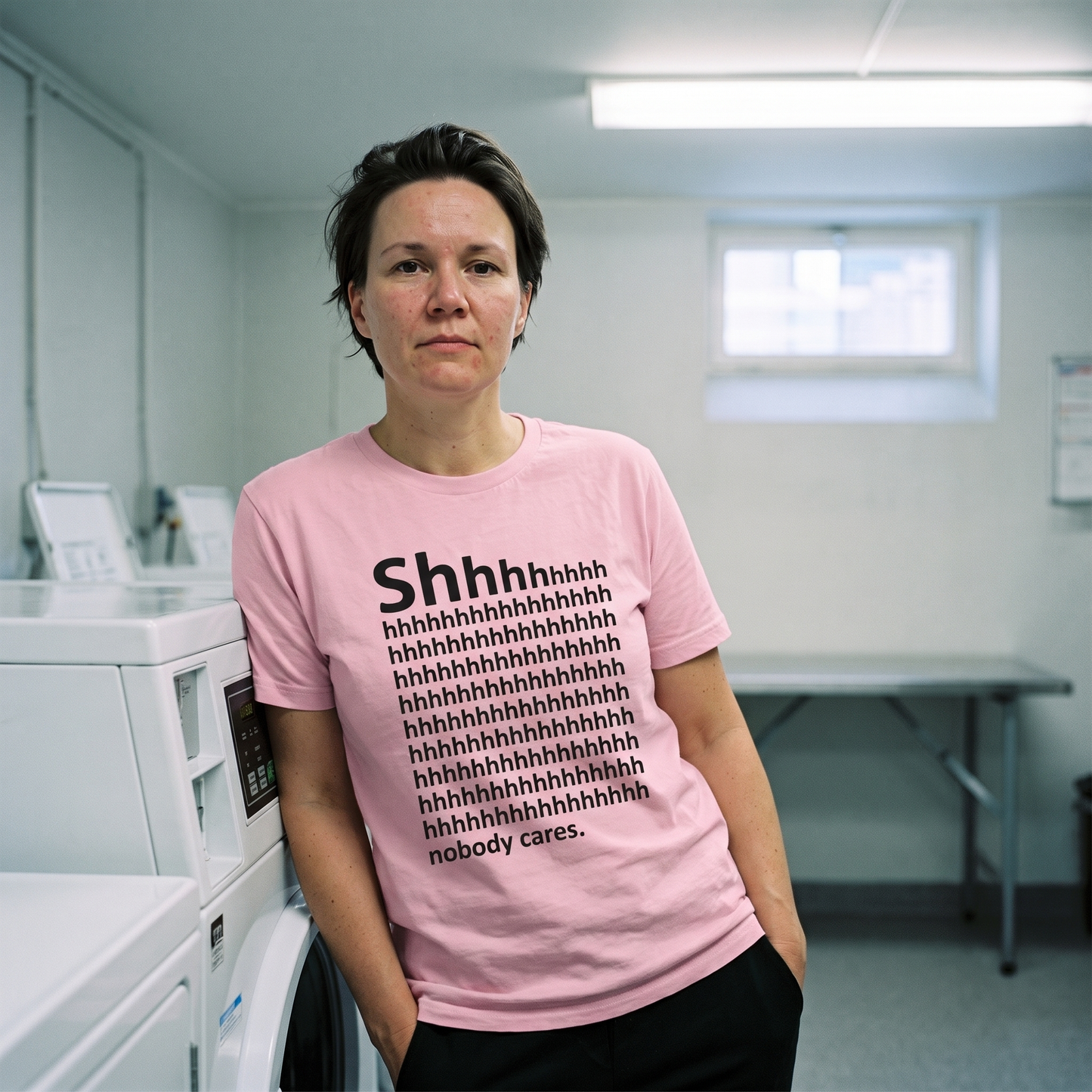 Shhh... Nobody Cares t-shirt in pink, worn by a woman in a laundry room, Very Finnish Problems