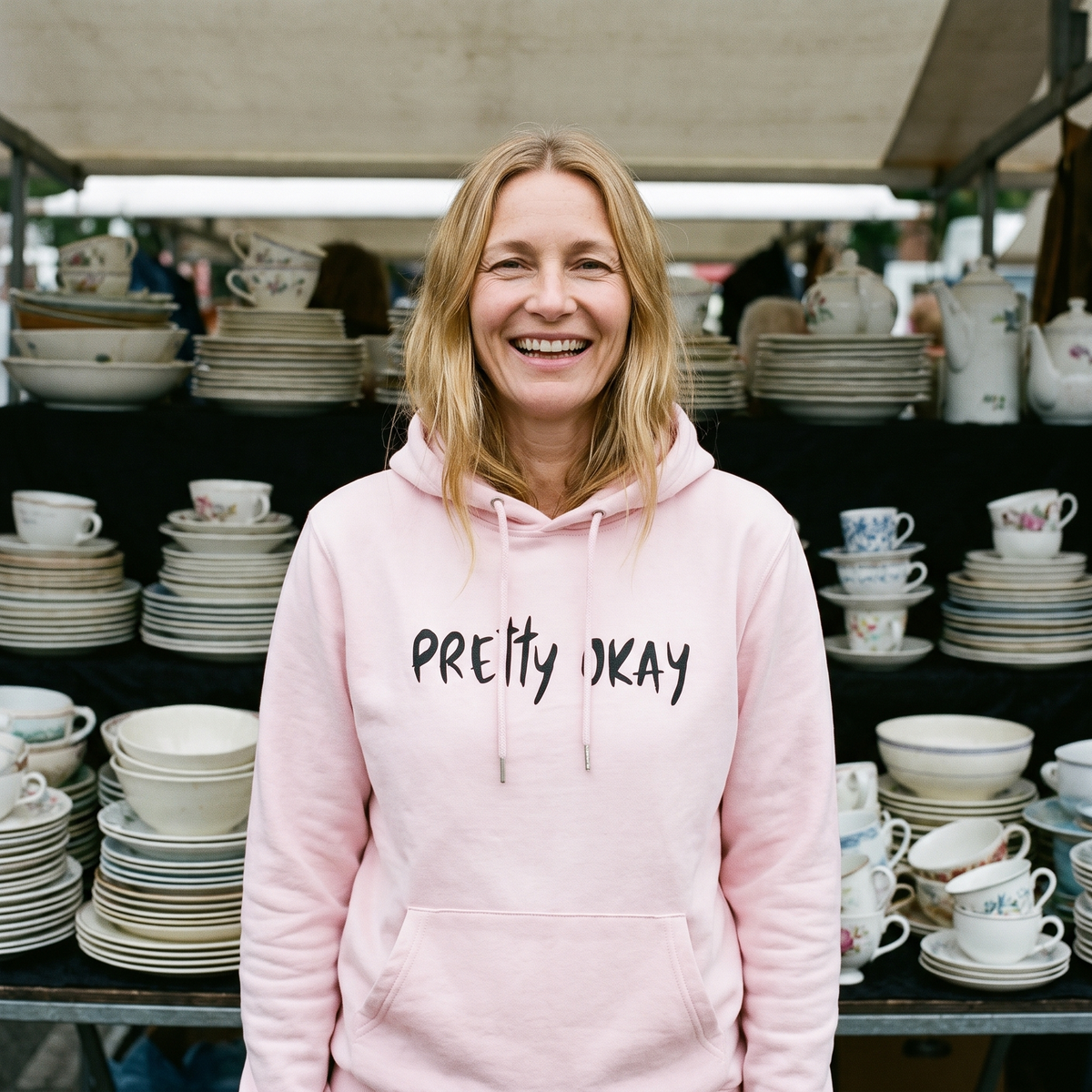 Pretty okay Finnish humour hoodie in light pink, worn by Elina at a flea market stall, Very Finnish Problems
