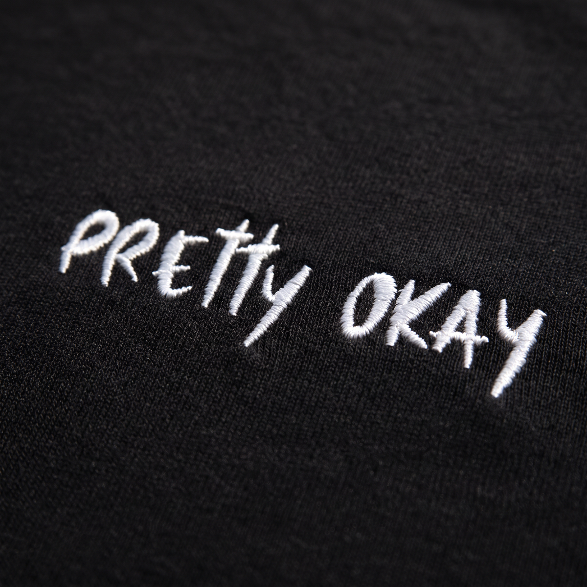 Close-up of the pretty okay embroidery stitched in white thread on black fabric, Very Finnish Problems