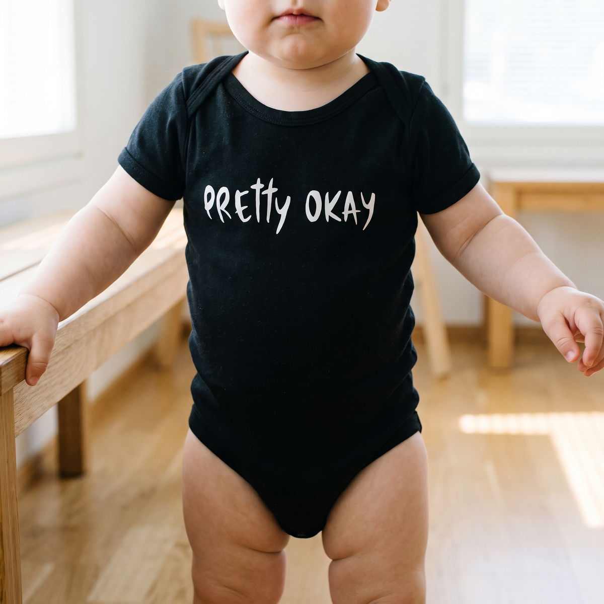 Pretty okay Finnish baby bodysuit in black, worn by a baby holding a bench, Very Finnish Problems