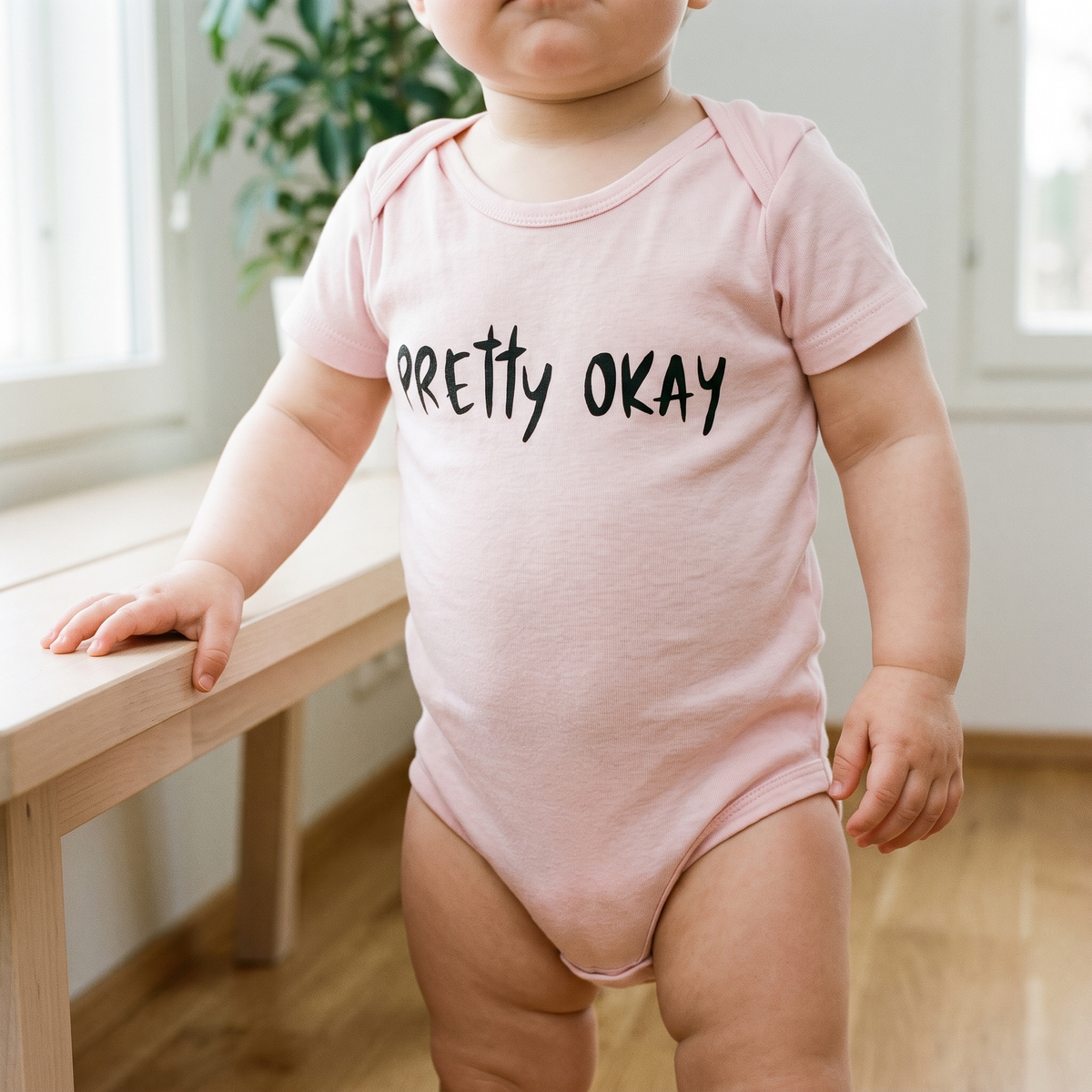 Pretty okay Finnish baby bodysuit in pink, worn by a baby holding a bench, Very Finnish Problems