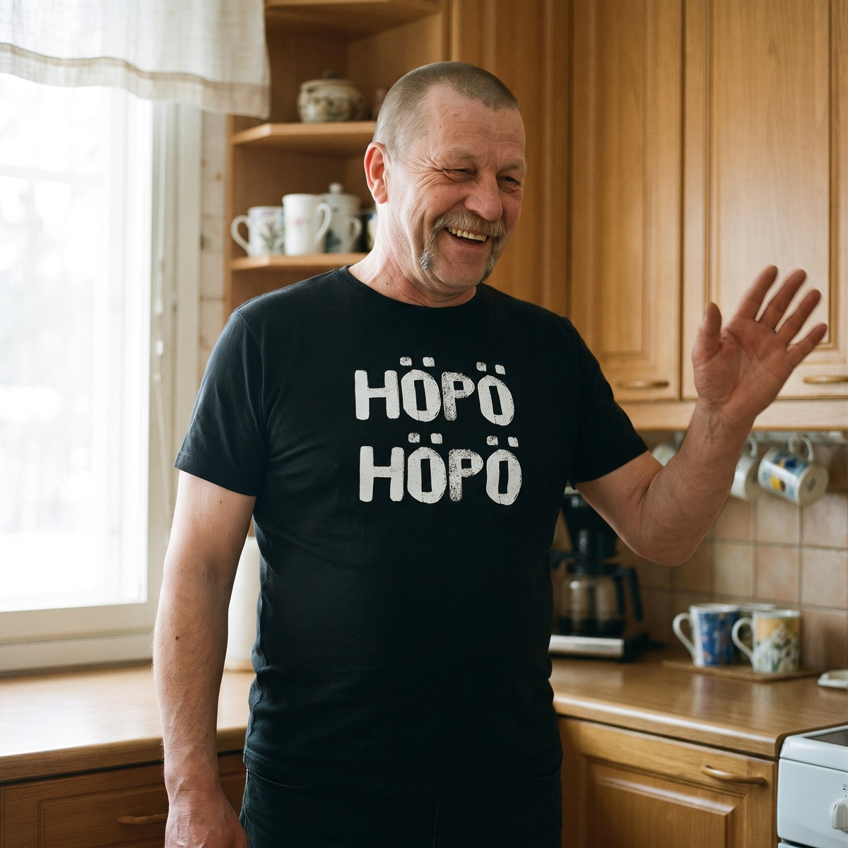 Höpö höpö Finnish language t-shirt in black, worn by a man laughing and waving something away in a kitchen, Very Finnish Problems