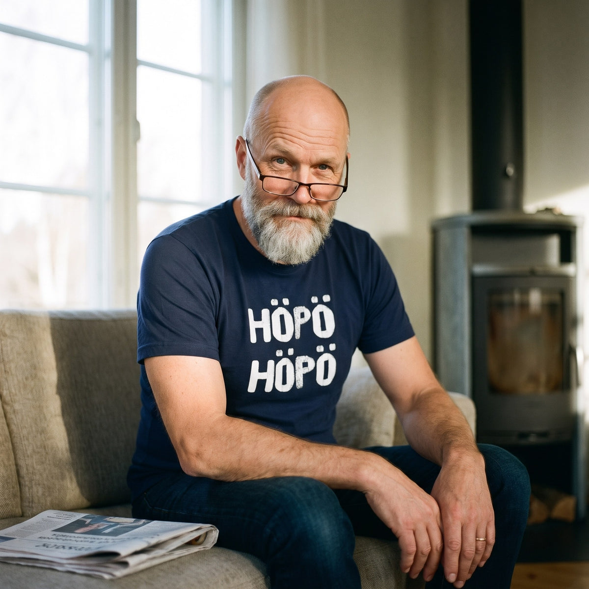 Höpö höpö Finnish language t-shirt in navy, worn by a man raising an eyebrow over his reading glasses on a sofa, Very Finnish Problems