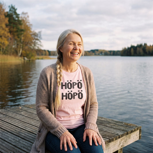Höpö höpö Finnish language t-shirt in pink, worn by a woman laughing on a lakeside jetty, Very Finnish Problems