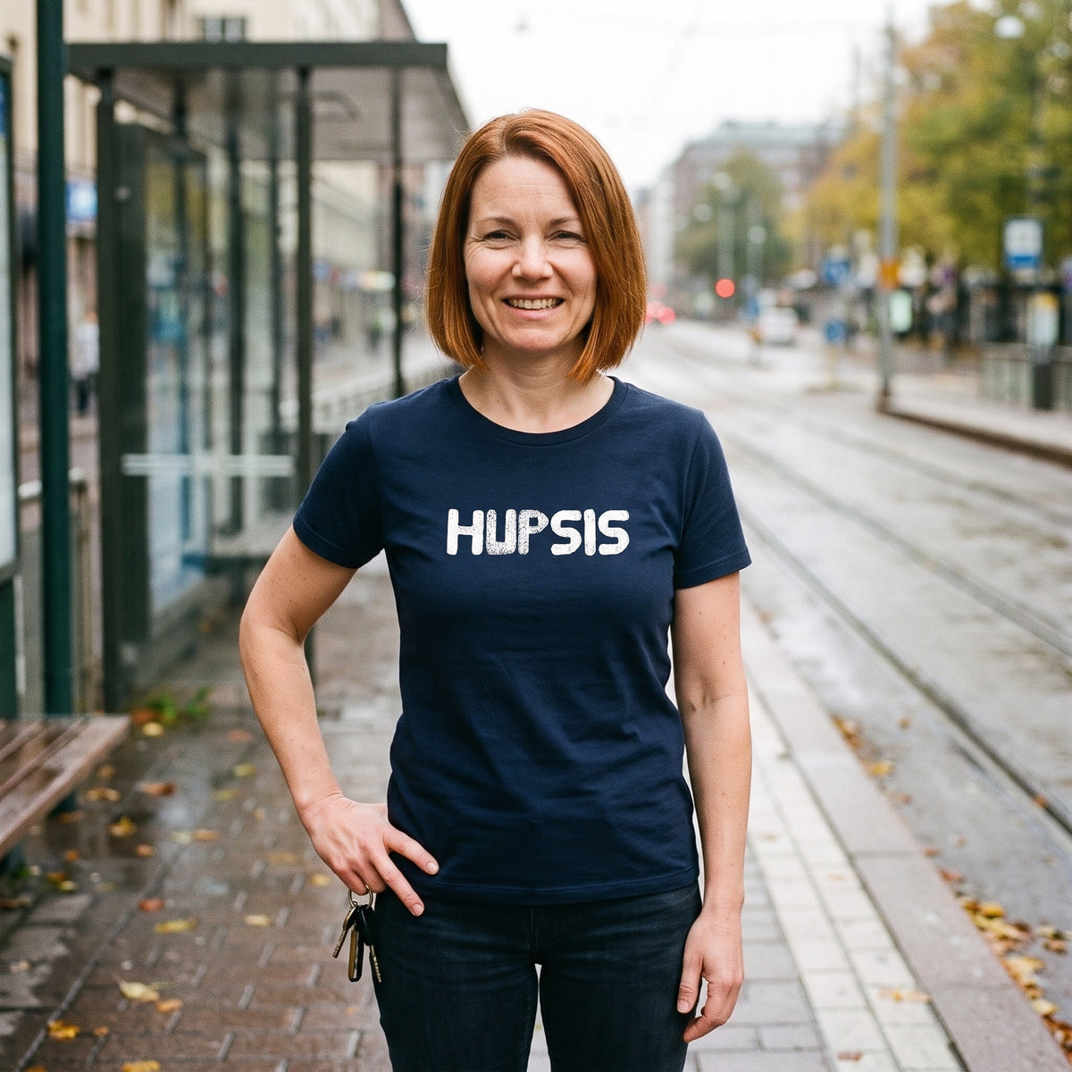 Hupsis Finnish language t-shirt in navy, worn by a woman wincing as she picks up dropped keys at a tram stop, Very Finnish Problems