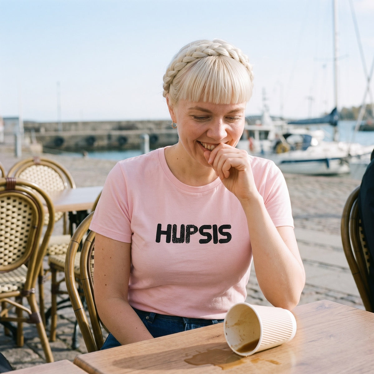 Hupsis Finnish language t-shirt in pink, worn by a woman with a hand to her mouth beside a spilled coffee, Very Finnish Problems