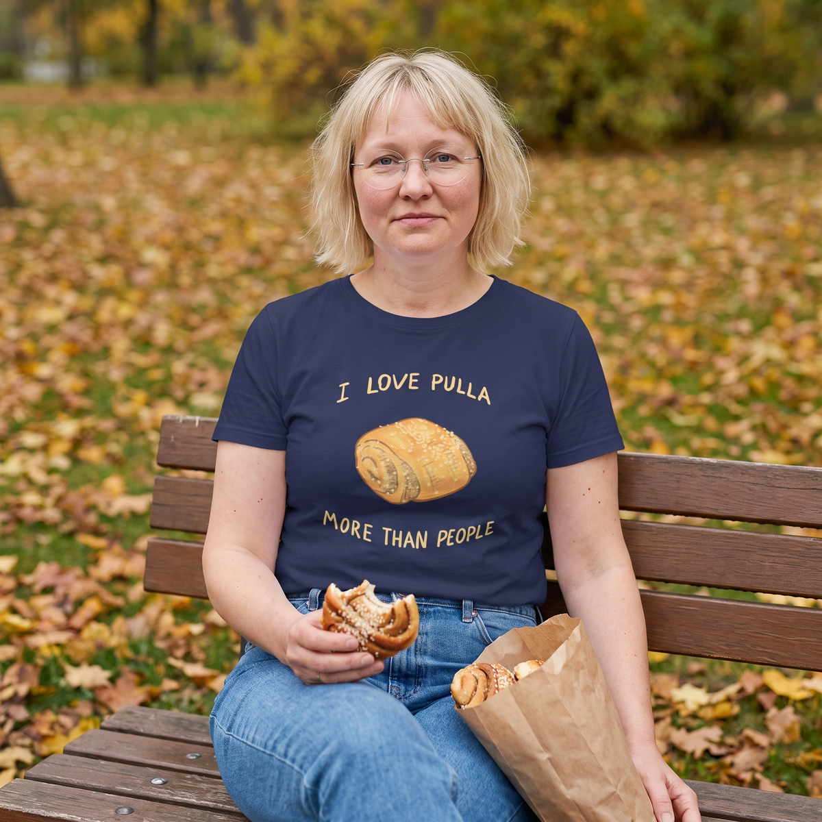 I Love Pulla More Than People t-shirt in navy, worn by Marika with a bag of pulla on a park bench, Very Finnish Problems