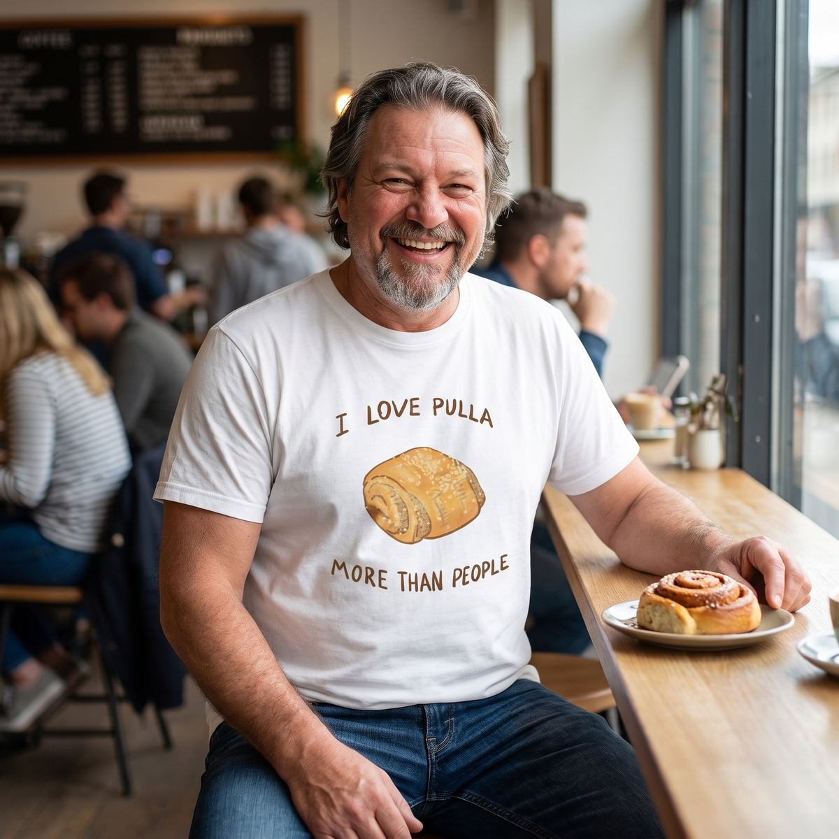 I Love Pulla More Than People t-shirt in white, worn by Jojelli alone with a cinnamon bun in a busy cafe, Very Finnish Problems