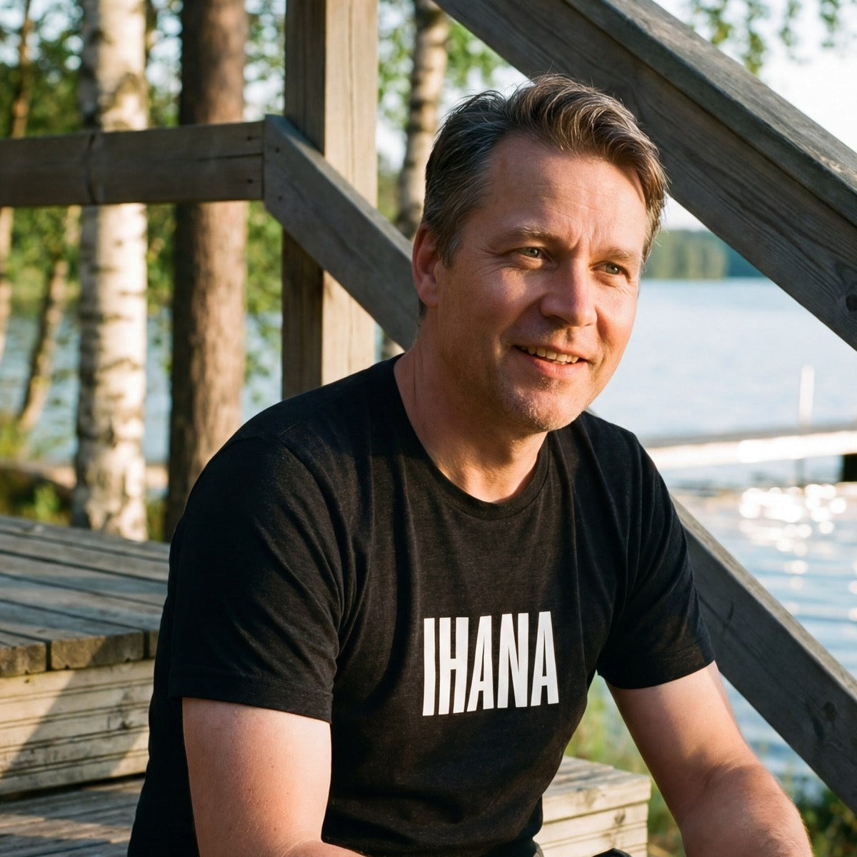 Man at a Finnish summer cottage by the lake wearing the IHANA Finnish t-shirt in black