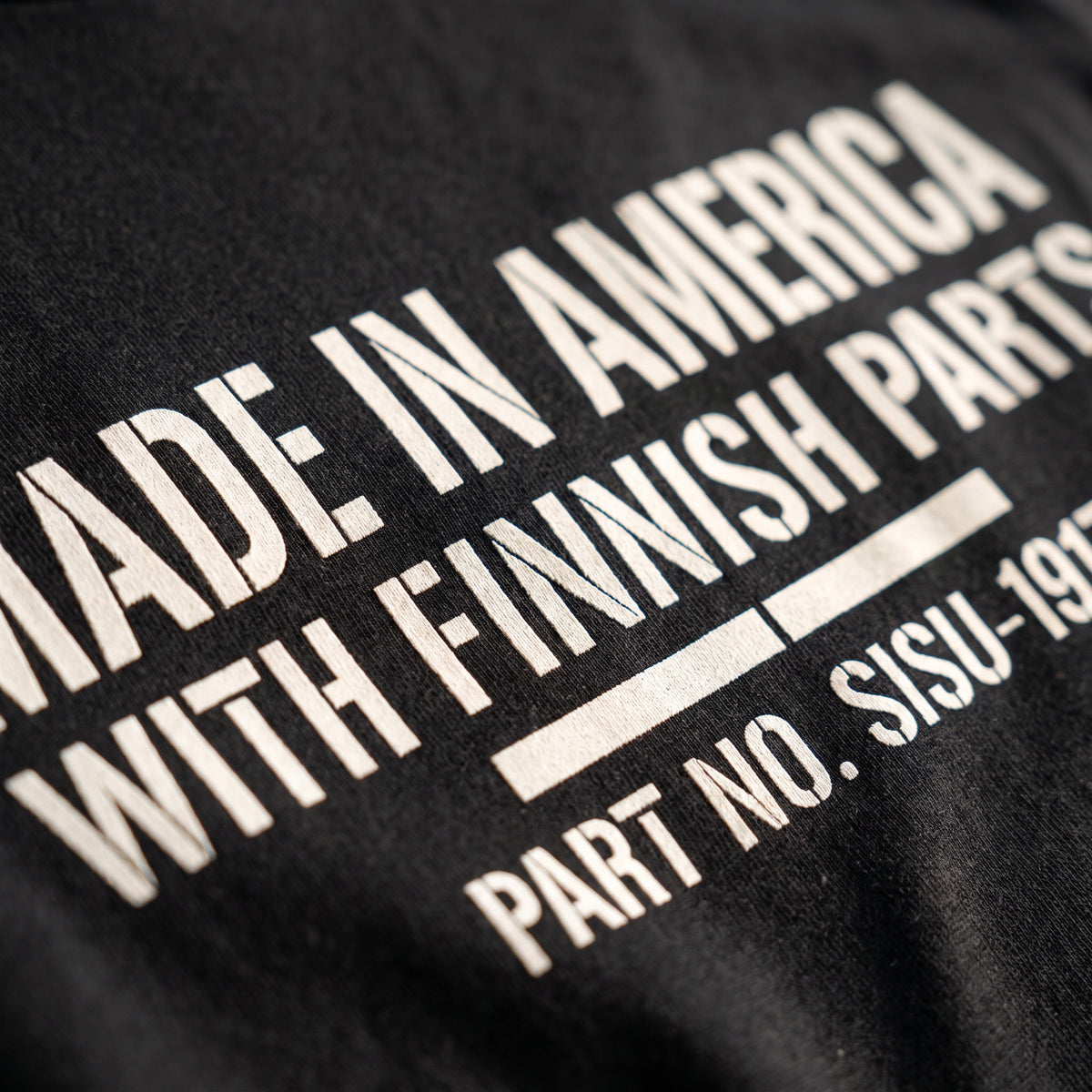 Close-up of the Made in America with Finnish Parts stencil print on black cotton, Very Finnish Problems
