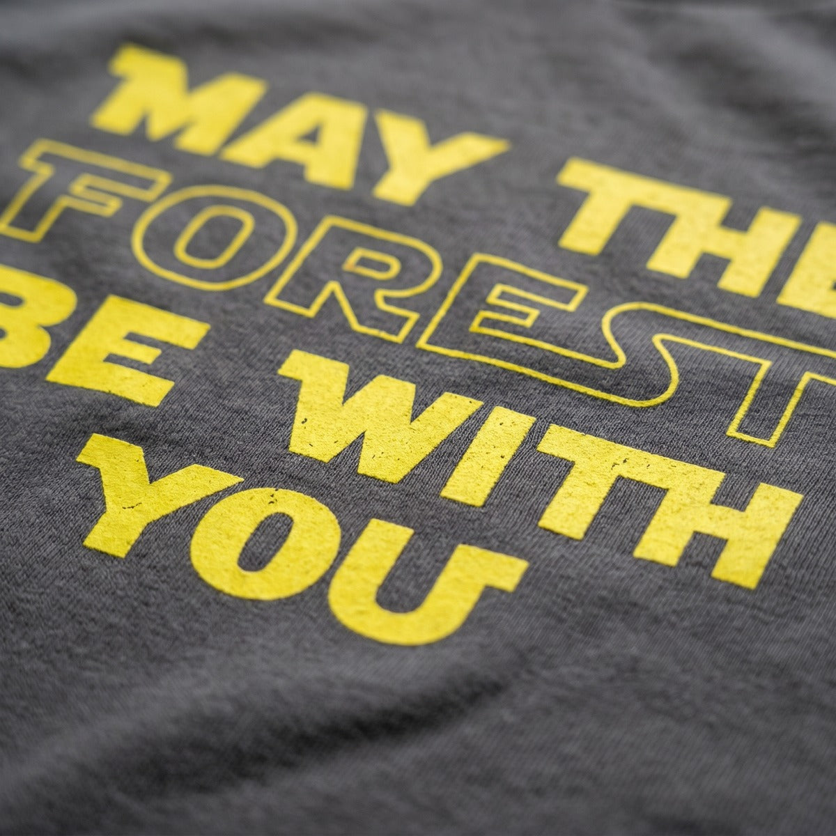 Close-up of the yellow May the Forest Be with You print on an asphalt grey t-shirt, Very Finnish Problems