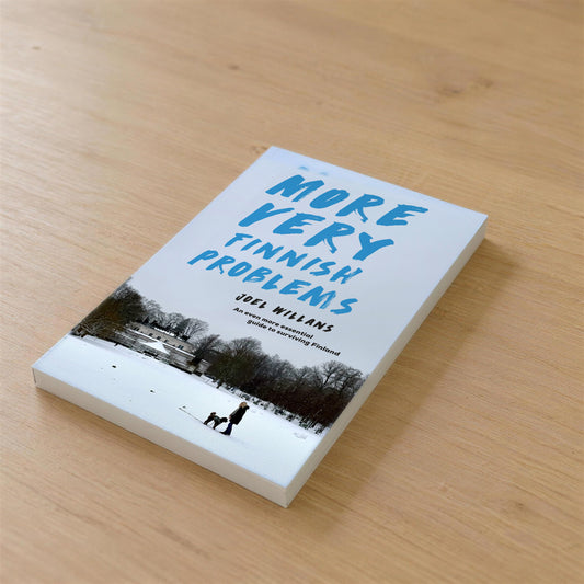 Front cover of More Very Finnish Problems by Joel Willans, the paperback lying on a wooden kitchen table