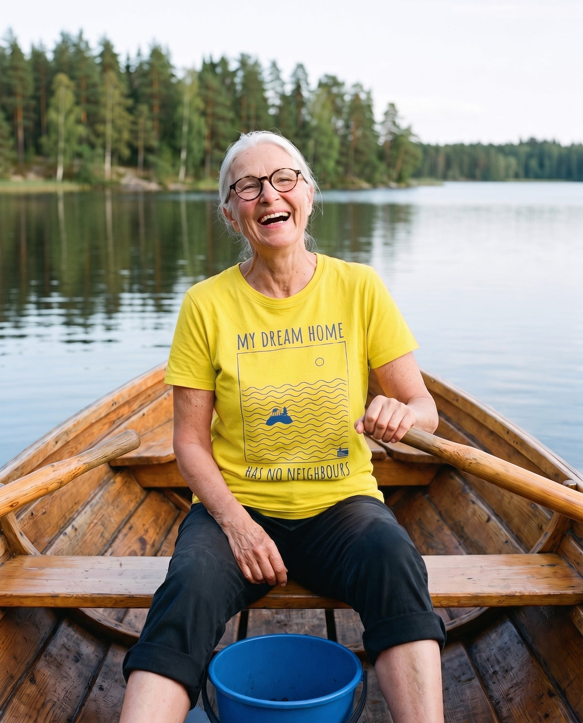 No Neighbours t-shirt in yellow, worn by Raija laughing in a rowing boat on a still Finnish lake, Very Finnish Problems