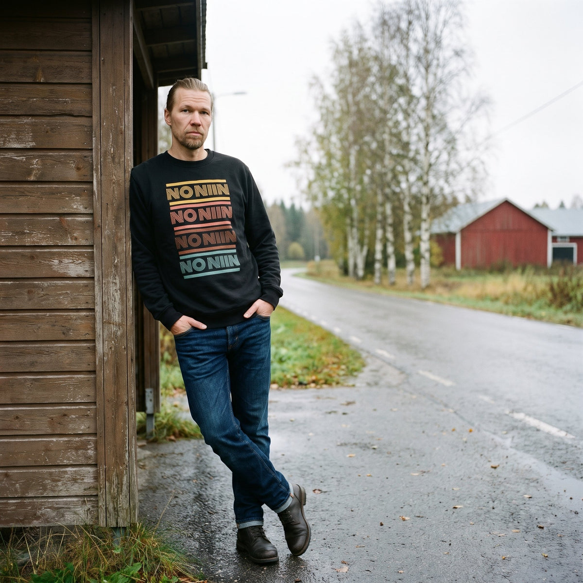 No niin retro sweatshirt in black, worn by a man with a blond beard leaning on a wooden bus shelter by a Finnish country road, Very Finnish Problems