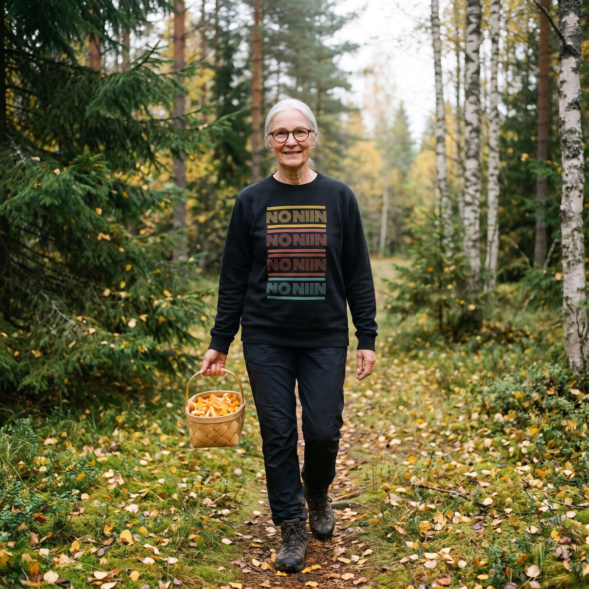 No niin retro sweatshirt in black, worn by a woman with silver hair and round glasses carrying a basket of chanterelles along a Finnish forest path in autumn, Very Finnish Problems