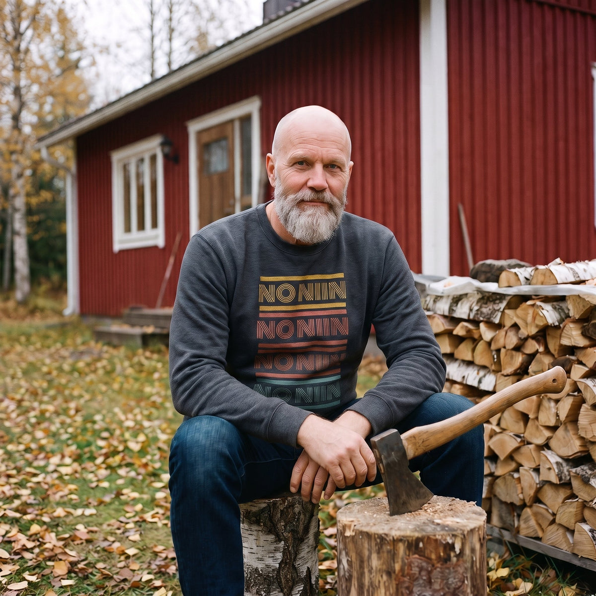 No niin retro sweatshirt in dark heather, worn by a bearded man sitting on a chopping block by a woodpile at a red Finnish cottage, Very Finnish Problems